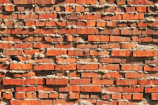 This rugged red brick wall exhibits extruded mortar and an irregular surface.