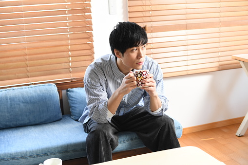 Young Asian man drinking a drink while sitting on the sofa