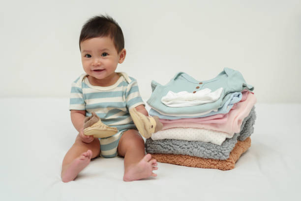istock happy infant sitting with stack of baby clothes on bed 1795997395