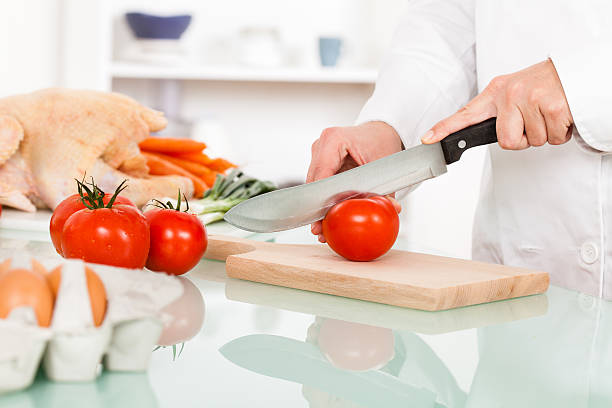 Chef cutting tomatos in the kitchen, preparing meal.