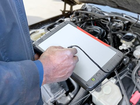 Auto mechanic using car diagnostic tool in front of a car engine