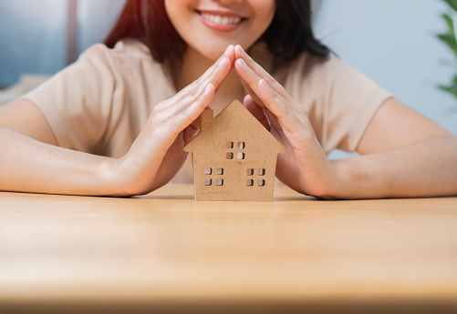 Happy Asian woman hands over house model for protection and care. Property insurance concept. Close up, copy space. Selective focus on hands