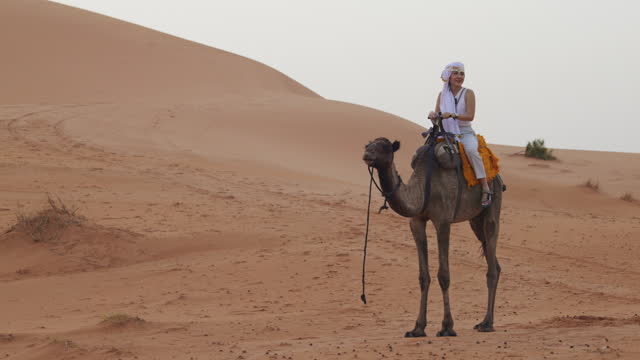 A female tourist enjoy the experience of camel riding explore the Sahara desert.