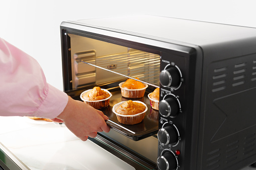 Woman's hands taking buscuit cupcakes out of mini oven closeup