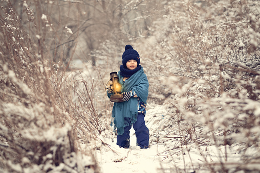 A little boy plays with the snow, rejoices in the snow and carries his flashlight through the forest to Santa Claus.