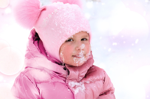 Cute baby girl with snow on her face, vacations, funny winter game outdoors