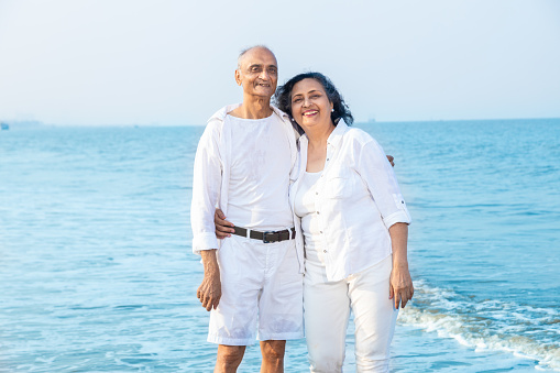 Happy senior indian couple wearing white cloths enjoying summer vacation, holiday at beach.