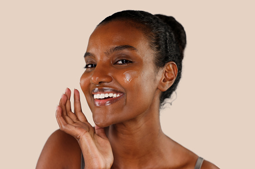 Young cheerful african american woman in skincare and beauty routine studio shoot, applying lotion,  moisturizer