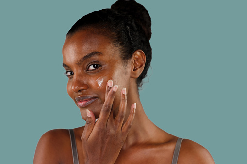 Young beautiful African American woman in skincare and beauty routine studio shoot,  applying lotion,  moisturizer