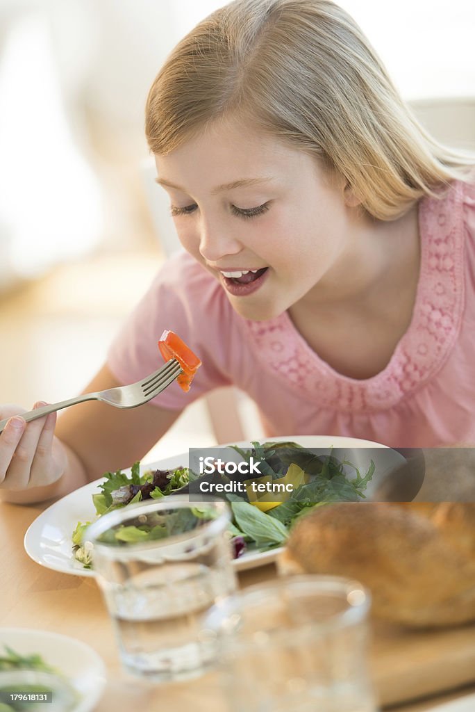 Girl Eating Salad At Dining Table Little girl eating fresh salad at dining table 10-11 Years Stock Photo