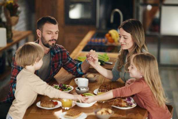 Young family praying before breakfast at dining room.