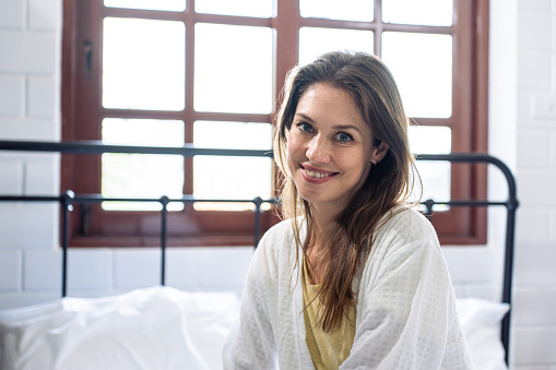 Portrait of Caucasian young girl in pajamas smile and look at camera. Attractive beautiful woman feeling fresh and happy to wake up from bed in bedroom in morning at home. healthy lifestyle concept.