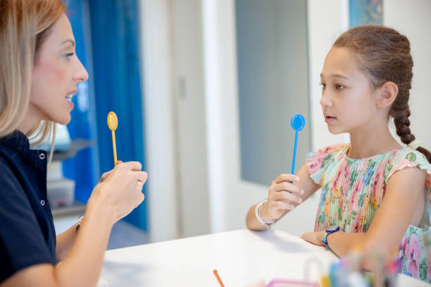 istock Elementary age girl holding special therapeutic aid and looking at speech therapist 1796205172