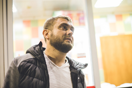 At night, a man stands near a brightly lit fast food cafe and waits for the food to be prepared. Portrait of a handsome man at night against the backdrop of a fast food restaurant window.