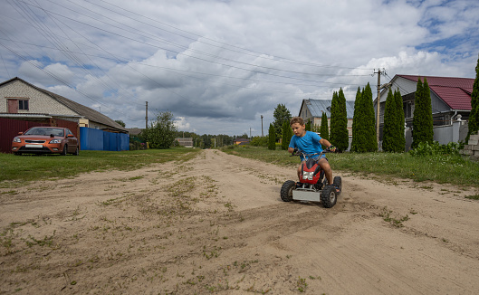 A child makes a sharp turn on an ATV, kicking up dust and sand from the road. The wheels of the ATV slip on the sand, raising dust and sand. A child boy enjoys riding an ATV.