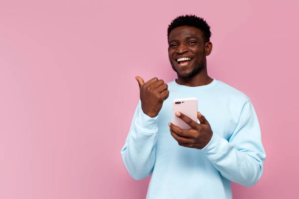 istock african american man in blue sweater uses smartphone and points to empty space on pink isolated background 1796245962