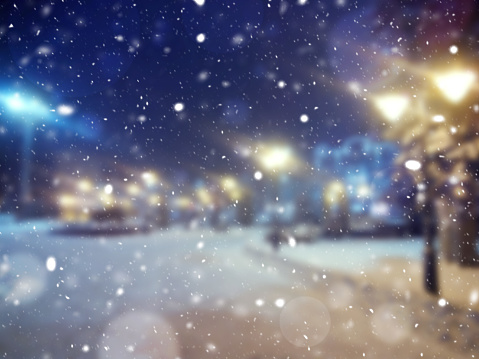 Blurred background. Winter in the city. Blizzard. Christmas Eve. Winter evening. Christmas scene with snowy streets. Christmas winter blurred background with garland lights, holiday festive background