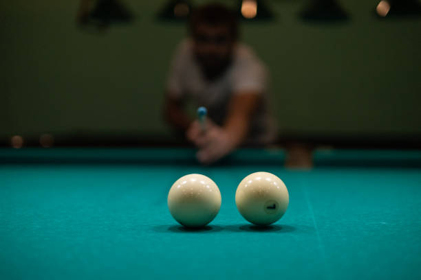 istock A man plays billiards and prepares to hit. A man aims his cue at a billiard ball while leaning towards the table. In the evening, a man relaxes after work by playing billiards. 1796268552
