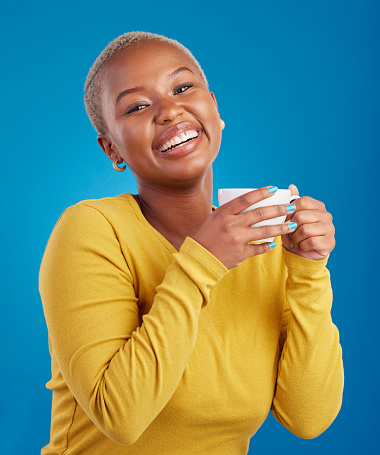 Black woman, happy and coffee or tea portrait in studio with a smile and happiness. African female model with a drink and hands on cup to relax with a positive mindset on blue background with beauty