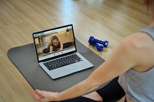 Young woman sitting on yoga mat watching active sports workout video lesson on laptop.