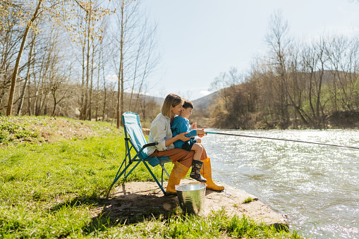 Photo of a little boy and his mother spending quality time together while fishing on the riverbank