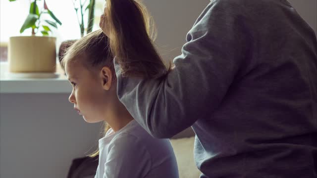 Shooting style is timelapse. Mom combs her daughter at home and makes her two ponytails. Happy childhood. Hair care