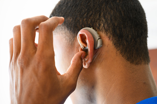 Close up side view young man putting hearing aid in ear