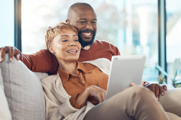istock Senior black couple, tablet on sofa or reading social network, email or communication with smile. Mature black woman, happy black man on mobile technology and social media, relax on web app in home 1796395239