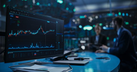 Close Up on a Computer Screen with Real-Time Stock Market Analytics, Graphs and Reports. Stock Exchange Software Template. Brokers Discussing Financial and Business Opportunities in the Background