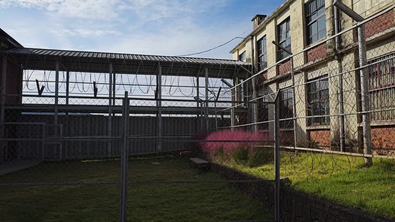 Old Prison Yard Barbed Wire Fence and Jail Building on Sunny Day