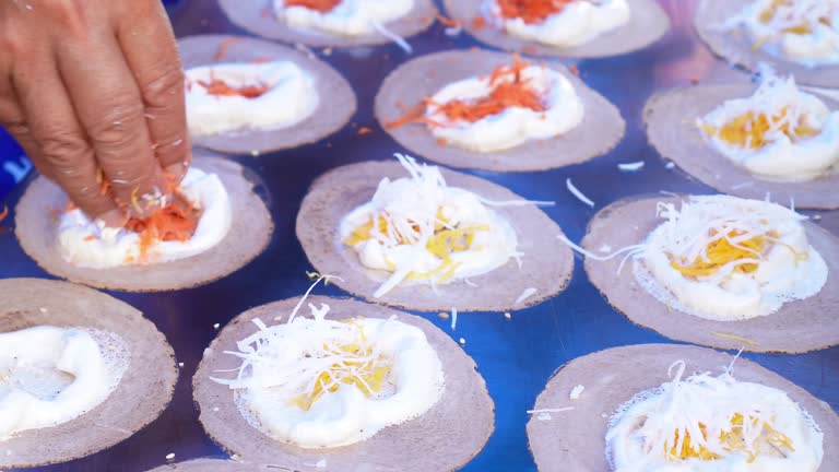 Video footage while the chef spreads the prepared strips of egg yolks filling onto a circle of fried dough on a hot pan, Thai crispy pancakes topped with strips of egg yolks, step 3.