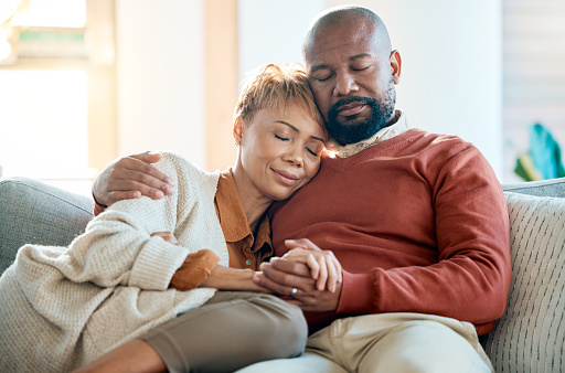 Love, relax and trust with a black couple on a sofa in the living room of their home together. Hug, marriage and romance with a mature man and woman bonding in the lounge of a house during the day