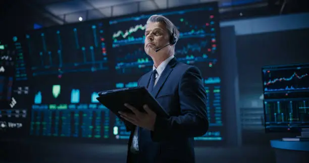 Professional Stock Exchange Trader Working on a Tablet Computer. Middle Aged Stockbroker Buying and Selling Shares During Day Trading. Businessman Analyzing Financial and Corporate Data