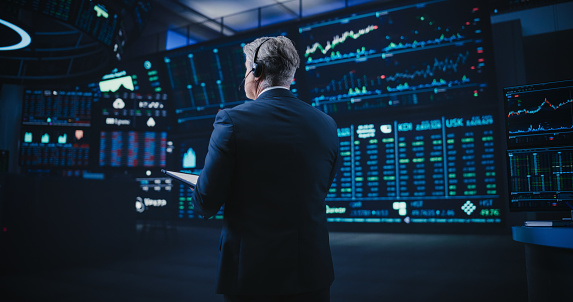 Concentrated businessman trader looking at pc monitor with diagram of stock crypto currency market, pointing with pen at screen, touching chin analyzing tendency of money flow, inventing new strategy