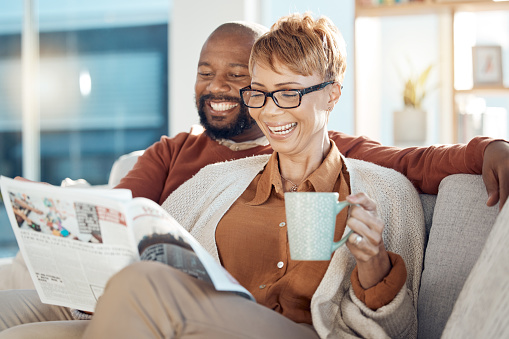 Coffee, sofa and senior couple with newspaper reading story or article while drinking espresso. Black couple, tea and happy man and woman relax in house, enjoying quality time together and bonding.