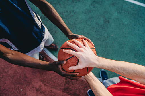 Two friends are holding a basketball ball at the pick-up basketball court. They are getting ready to start play basket. Focus on the hands holding the ball.