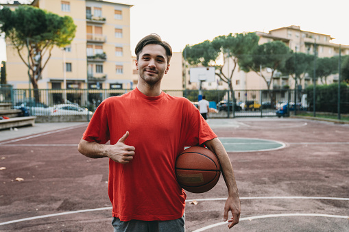 Portrait of a young adult man standing in a pick-up basketball court. He's looking at camera and smiling.