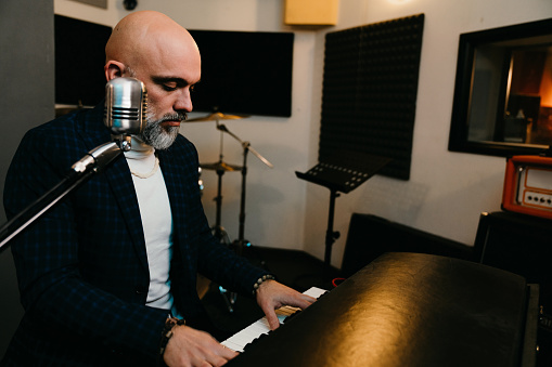 A musician is playing piano in a professional recording studio. He's playing and singing.