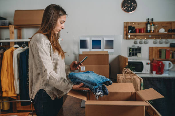 A millennial woman is preparing the shipment of some clothes in her new online shop A millennial woman is preparing the shipment of some clothes in her new online shop. She's the owner of an online thrift store. New small business concept. wholesale work pants stock pictures, royalty-free photos & images