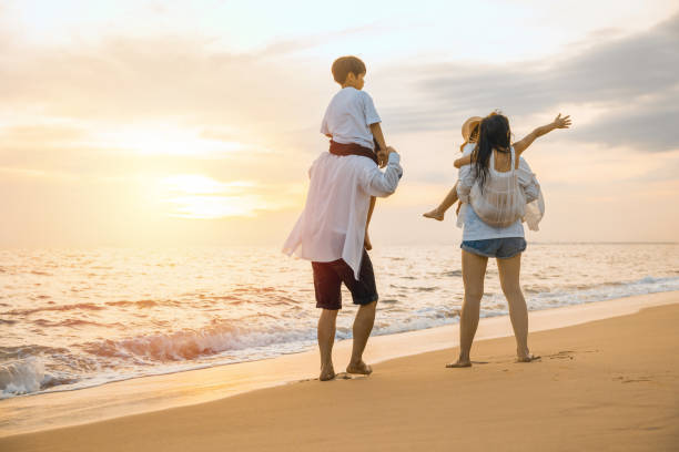 istock Parents carrying children on shoulders at beach on sunset 1796419475