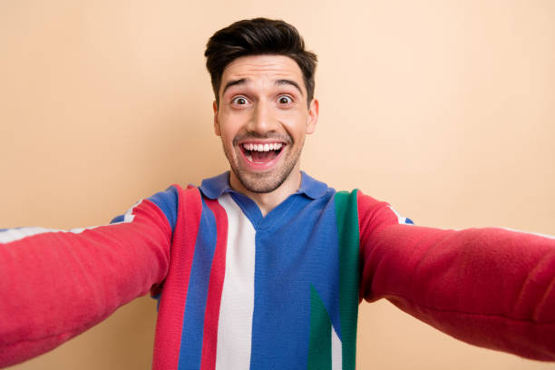 selfie cadre of positive funny young vlogger man holding camera recording his good mood laughing isolated on beige color background - bizarre making a face men one person imagens e fotografias de stock