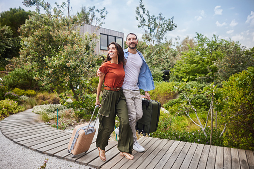 Smiling couple walking with suitcases after arriving at their scenic vacation rental in the summertime