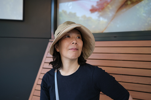 Smiling Asian woman with hat on a bench outdoors, looking up.
