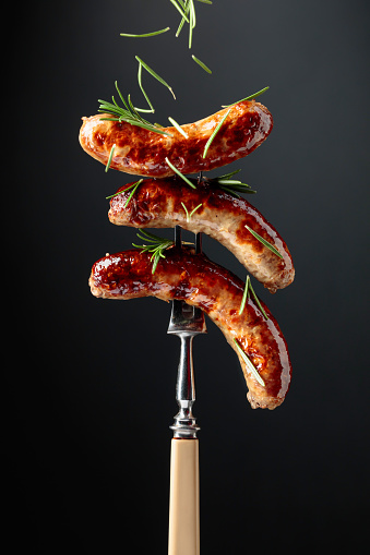 Grilled Bavarian sausages with rosemary.  Sausages  on a fork sprinkled with rosemary.