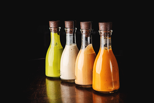 Set of glass bottles with different delicious craft sauces on black background