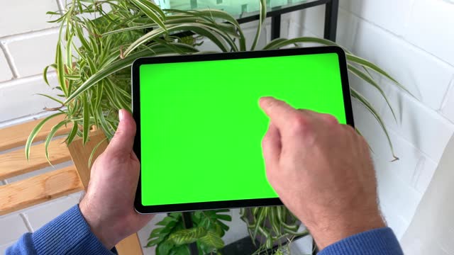 Close up Mans hands Holding Tablet Computer with Green Screen Mock Up Display. Relaxing at Home