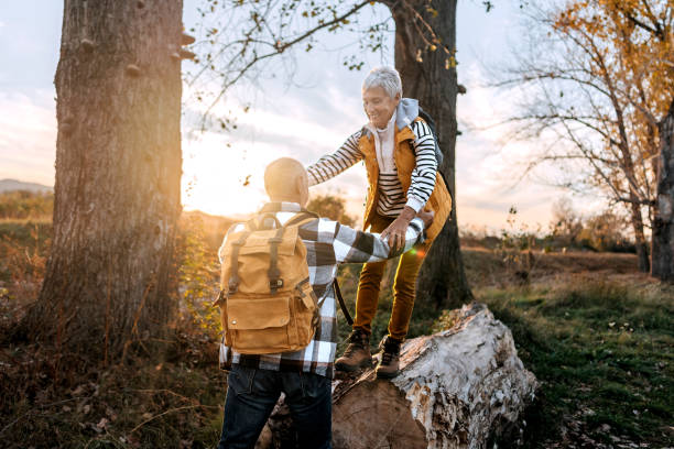 istock Senior man helping his wife to walk on a tree log in forest 1796498475