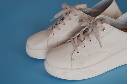 Universal women's beige light leather sneakers with laces on a blue background. Fashionable street shoes.