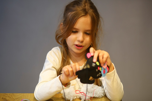 Indoor portrait of a girl sewing a toy, art and craft