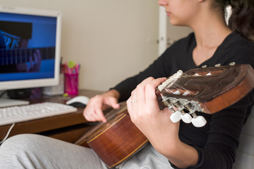 Young Girl watching online guitar lesson on computer.